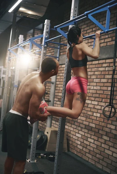 Træner hjælper kvinde med pull ups - Stock-foto