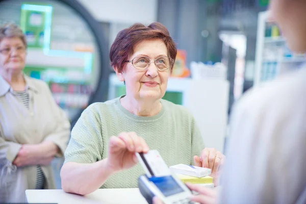 Mulher sênior que paga com cartão de crédito em farmácia — Fotografia de Stock