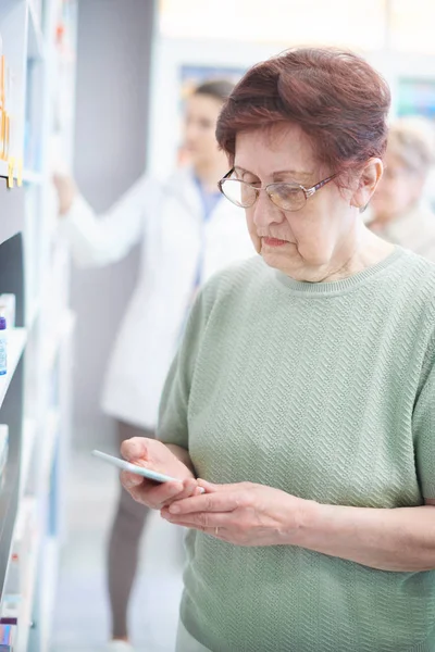 Mature woman using smartphone in drug store — Stock Photo, Image