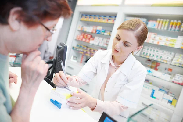 Joven farmacéutico ayudando a clientes mayores — Foto de Stock