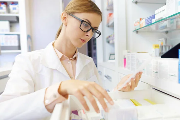 Femeie farmacist răsfoire medicamente pe raft — Fotografie, imagine de stoc
