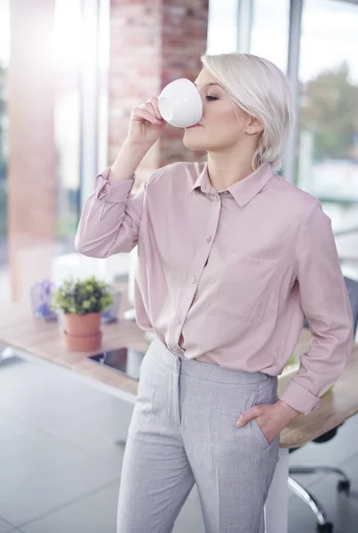 Mulher com a mão nos bolsos tendo um café — Fotografia de Stock