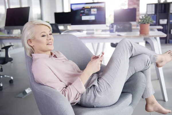 Barefoot businesswoman lying on armchair with mobilephone