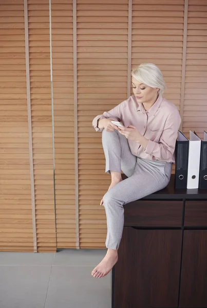 Barefoot woman sitting on drawer and texting