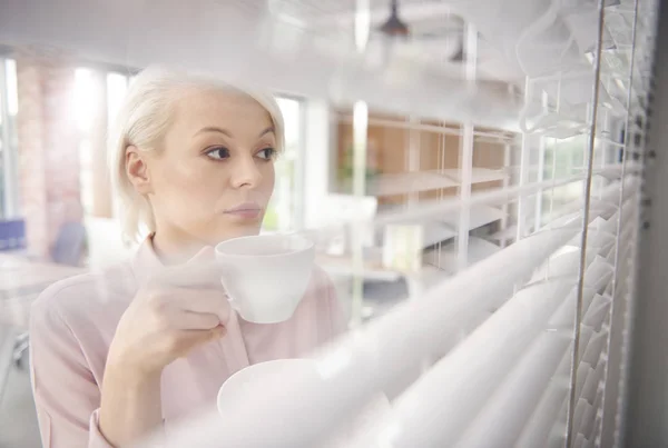 Femme d'affaires avec café regardant à travers les stores — Photo