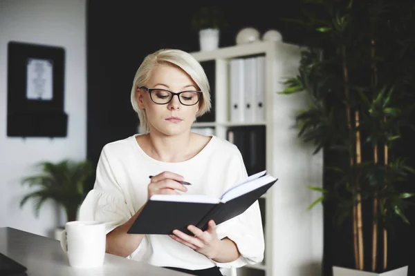 Fokussierte Frau schreibt in ihrem Büro an einem Notizbuch — Stockfoto