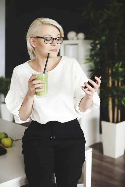Vrouw met smoothie texting op het werk — Stockfoto
