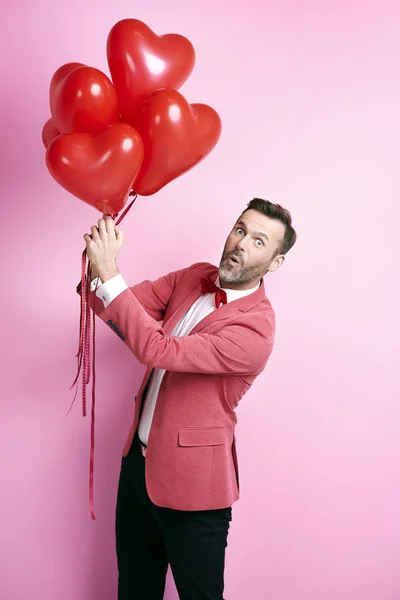 Surprised man holding heart shape balloons — Stock Photo, Image