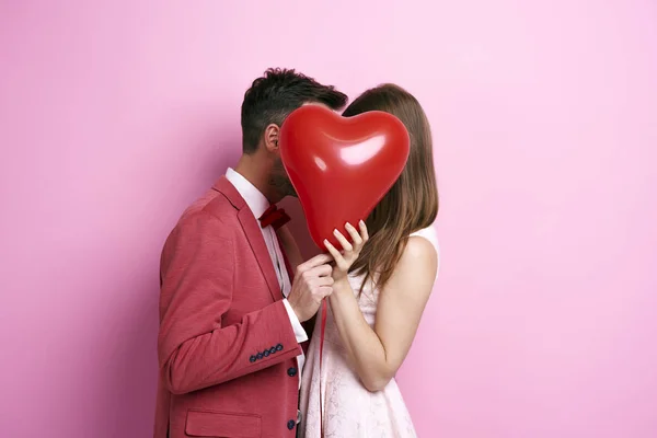 Affectionate couple covering face with balloon and kissing — Stock Photo, Image