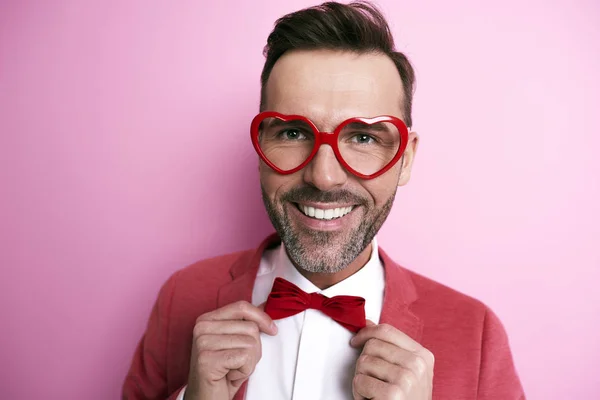 Hombre alegre con gafas en forma de corazón ajustando una pajarita —  Fotos de Stock