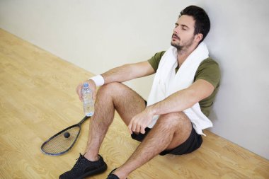 Katta oturan genç erkek squash oyuncu yorgun 