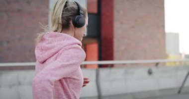 Sportif bir kadın şehirde koşuyor ve müzik dinliyor.