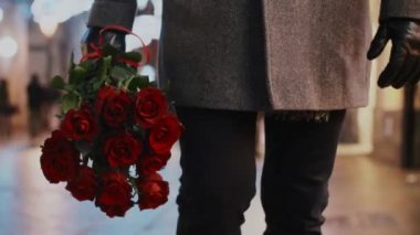 Bir demet kırmızı gül tutan adamın alçak kesimi.