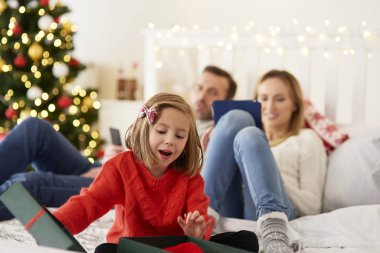 Hediyeyi açan çocuk ve arka planda teknolojisi olan aileler. 