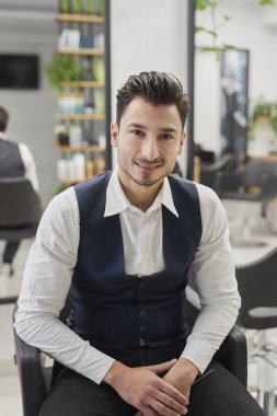 Kuaförde oturan gülümseyen erkek müşterinin portresi.