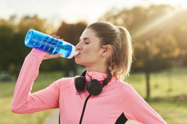 Woman taking a sip of refreshing water after jogging training
