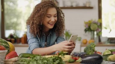 Genç bir kadın mutfakta cep telefonu kullanıyor.