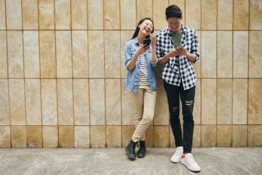 Duvarda cep telefonu olan genç bir çift var. 