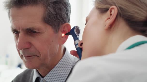 シニア男性の耳を調べる女性医師のハンドヘルドビュー 8Kで赤いヘリウムカメラで撮影 — ストック動画