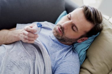 Yüksek ateşi olan hasta bir adam yatakta kalıyor.