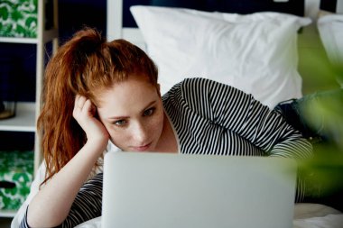 Yatakta dizüstü bilgisayar kullanan sıkıcı bir kadın.