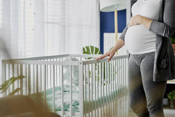 Pregnant woman standing next to a crib