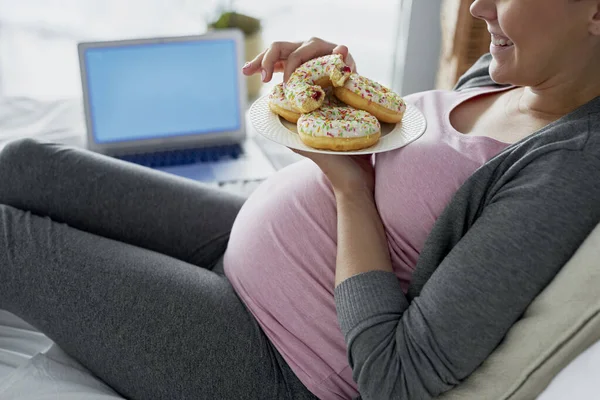 幸せな妊娠中の女性はベッドでドーナツを食べる — ストック写真