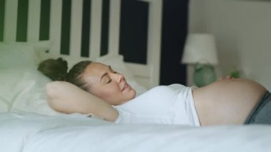 Yatakta rahatlayan neşeli hamile kadının el kamerasıyla çekilmiş videosu. 8K 'da kırmızı helyum kamerayla çekildi.  