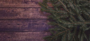 Koyu kahverengi ahşap masanın yanında koyu yeşil bir ladin dalı uzanıyor. Yazı pankartı için yeri olan koyu renkli neşeli bir Noel havası