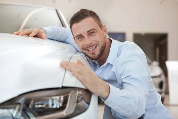 Handsome young man buying a new car at dealership salon