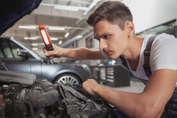 Jovem carro bonito mecânico reparando veículo em sua garagem — Fotografia de Stock