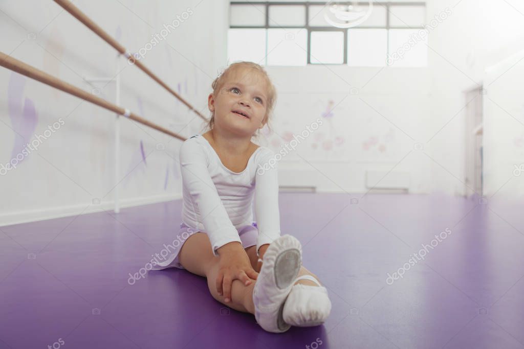 Cute happy little ballerina exercising at dancing school