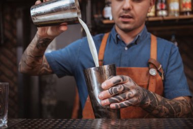 Yakışıklı erkek dövmeli barmen içki hazırlıyor.