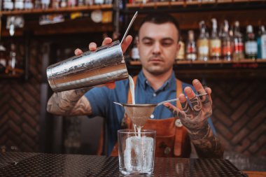 Yakışıklı erkek dövmeli barmen içki hazırlıyor.