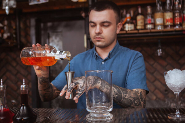 Handsome male tattooed bartender preparing a drink