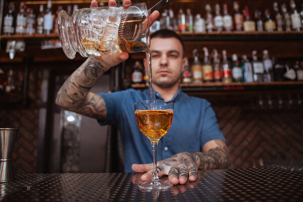 Handsome male tattooed bartender preparing a drink