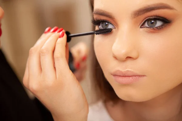 Cropped close up of professional makeup artist applying mascara on the lashes of a female client