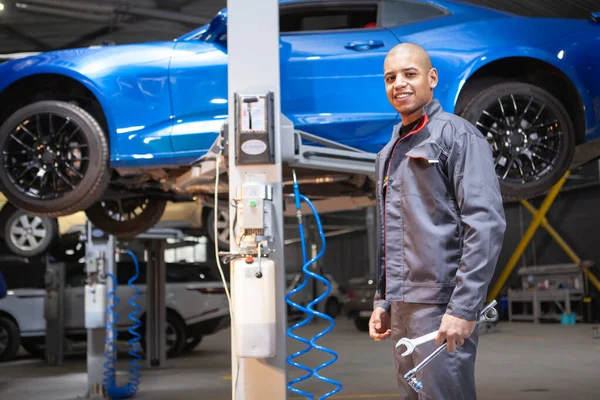 Cheerful handsome African male mechanic smiling to the camera confidently, working at car service