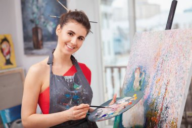 Atölyesinde resim yaparken kameraya gülümseyen mutlu güzel kadın. Sanat, yaratıcılık kavramı