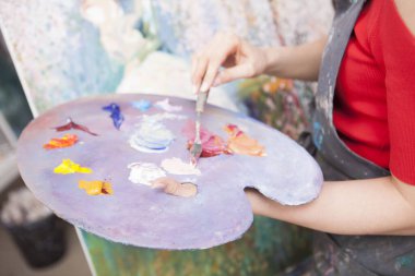 Yağlı boyaları karıştıran kadın ressamların olduğu bir paletin kapağı. Sanat stüdyosunda çalışan tanınmayan bir kadın.