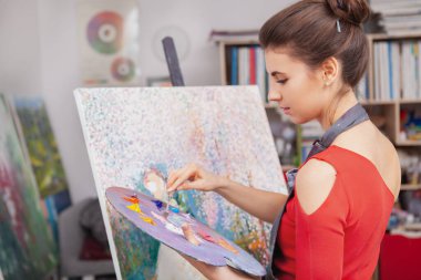 Sanat stüdyosunda çizim yapmak için yağlı boya kullanan çekici, zarif genç bir kadın. Meslek, mesleki kariyer kavramı