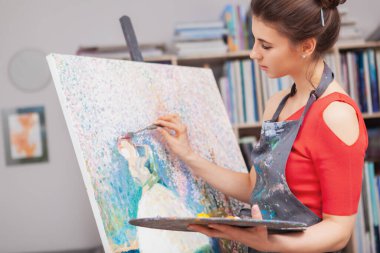 Stüdyosunda çalışan çekici kadın ressam yağlı boyayla tuvale resim yapıyor.