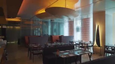 Masaları olan bir restoran, avizeleri ve büyük pencereleri olan parlak koltuklar.