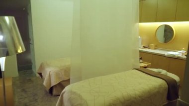 Baş destekli yatak, havlu perdeleri ve ahşap zemini olan koyu renk masaj odası.