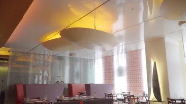Masaları olan bir restoran, avizeleri ve büyük pencereleri olan parlak koltuklar.