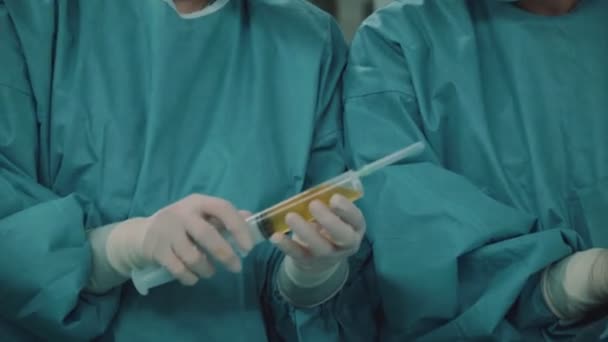 手术室里穿着医院长袍的女医生拿着一个装有药物的大注射器 — 图库视频影像