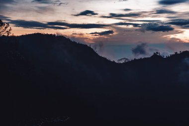 Endonezya 'daki Java Adası' ndaki bulutlar ve güneş ışınlarıyla dağlarda gün doğumunun karanlık bir fotoğrafı.