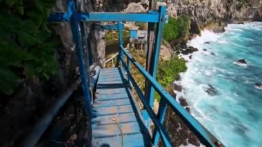 Eski ahşap merdivenlerde deniz ve kaya manzaralı yüksek bir dağdaki uçuruma uygun birinin videosu.
