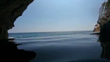 Yüksek bir dağdaki uçuruma uygun bir insanın deniz ve kaya manzaralı birinci şahıs videosu.