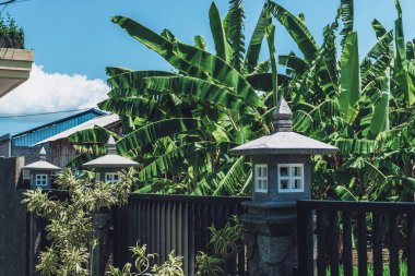 Dışarıda çitin üzerinde duran taştan yapılmış eski bir lambanın fotoğrafı.